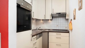Una cocina compacta con armarios blancos, un horno Bosch y un lavamanos.