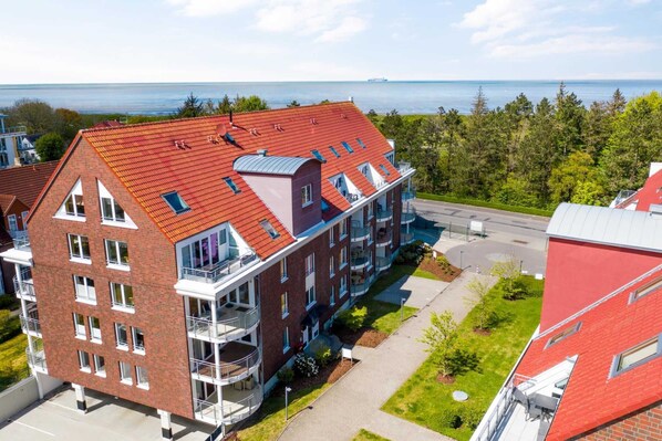Un immeuble résidentiel à plusieurs étages, doté d’un toit rouge, de balcons et offrant une vue sur la mer.