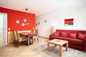 Un salon avec un canapé rouge, une table basse en bois et un coin repas comprenant une table et des chaises.