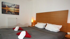 A hotel room with a large bed, a wooden headboard, a bedside lamp, and a painting of a sunset over the sea.