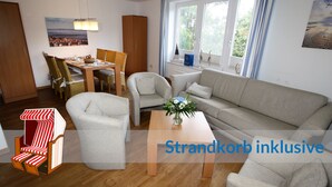 A furnished living room with a sofa, chairs, a dining table, and a view of the outdoors through large windows.