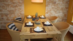 A dining table set for six with wicker chairs, a central fruit bowl, and a hanging light fixture.