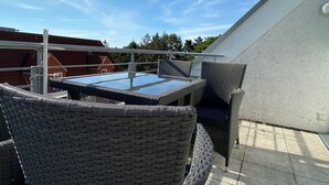 Eine Dachterrasse mit einem Glastisch und Korbstühlen, mit Blick auf ein Wohngebiet.
