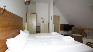 Ein Hotelzimmer mit einem großen Bett, einem Holzkopfstück, einem Fernseher, einem Sessel und einem Schreibtisch mit einem Computer.