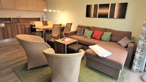 Ein modernes Wohnzimmer mit einer Couch, zwei Sesseln, einem Couchtisch und einem Essbereich mit Stühlen und einem Tisch.