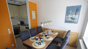 Uma sala de jantar com uma mesa de madeira, seis cadeiras e uma cozinha ao fundo.