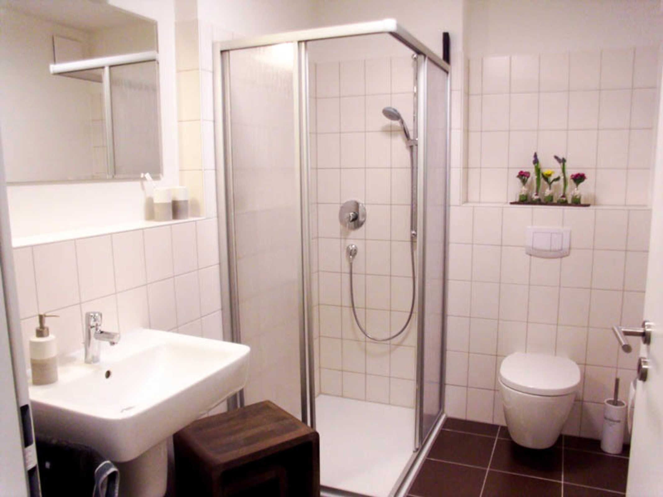 Et badeværelse med bruser, vask, toilet og en lille træskammel.