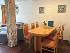 Un coin repas avec une table en bois, six chaises, un vase de fleurs et deux tableaux encadrés au mur.