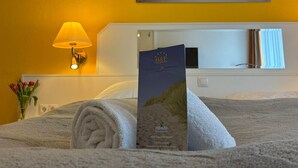 Une chambre d’hôtel avec un lit, une lampe, un tableau encadré et une brochure posée sur le lit.
