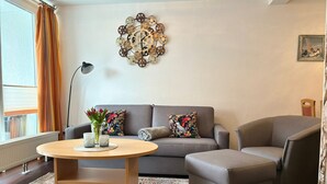 Un salon comprenant un canapé, un fauteuil, une table basse ronde et un élément décoratif mural.
