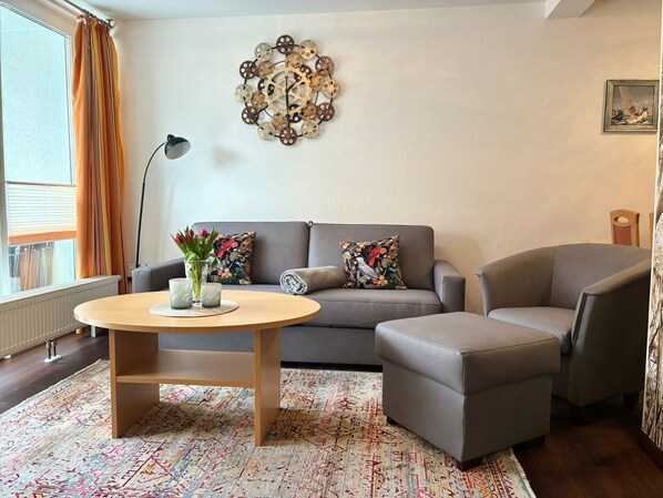 Un salon comprenant un canapé, un fauteuil, une table basse ronde et un élément décoratif mural.