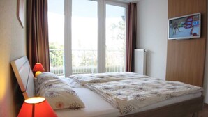 Een slaapkamer met een bed, een raam met gordijnen, een radiator en een televisie aan de muur.