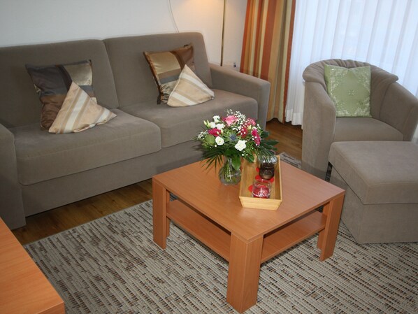 Una sala de estar con un sofá, una mesa de centro con un florero y una mesita auxiliar con velas.
