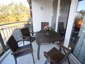 Un balcón con una mesa, cuatro sillas, un jarrón con flores y vistas a árboles y un edificio.