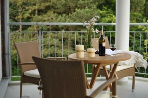 A balcony with wicker furniture, a round wooden table, candles, a bottle of wine, and a vase with flowers.
