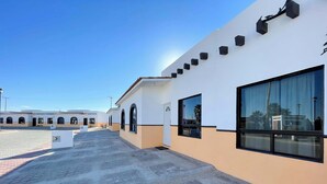 Un edificio con fachada blanca y ventanas grandes, un sendero pavimentado y un cielo azul despejado.