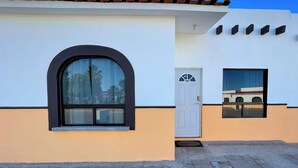 Un edificio con fachada blanca, techo de tejas marrones, un amplio ventanal arqueado, una puerta con un ventanuilla y una pequeña ventana rectangular.