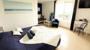 Ein Hotelzimmer mit Bett, Schreibtisch, Sessel, Fernseher und einem Fenster mit Vorhängen.
