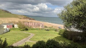 A coastal property with a grassy lawn, a wooden fence, and a view of the sea. - Beach Front Coastal Retreat with Sea Views (Kingsbridge)