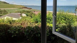 A coastal view with a house and a small shed, surrounded by greenery and a clear sky. - Beach Front Coastal Retreat with Sea Views (Kingsbridge)