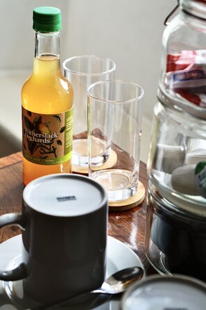 A table with a bottle of Witherslack Orchards apple juice, two clear glasses, a black mug, and a spoon. - The Derby Arms Witherslack (Grange-over-Sands)
