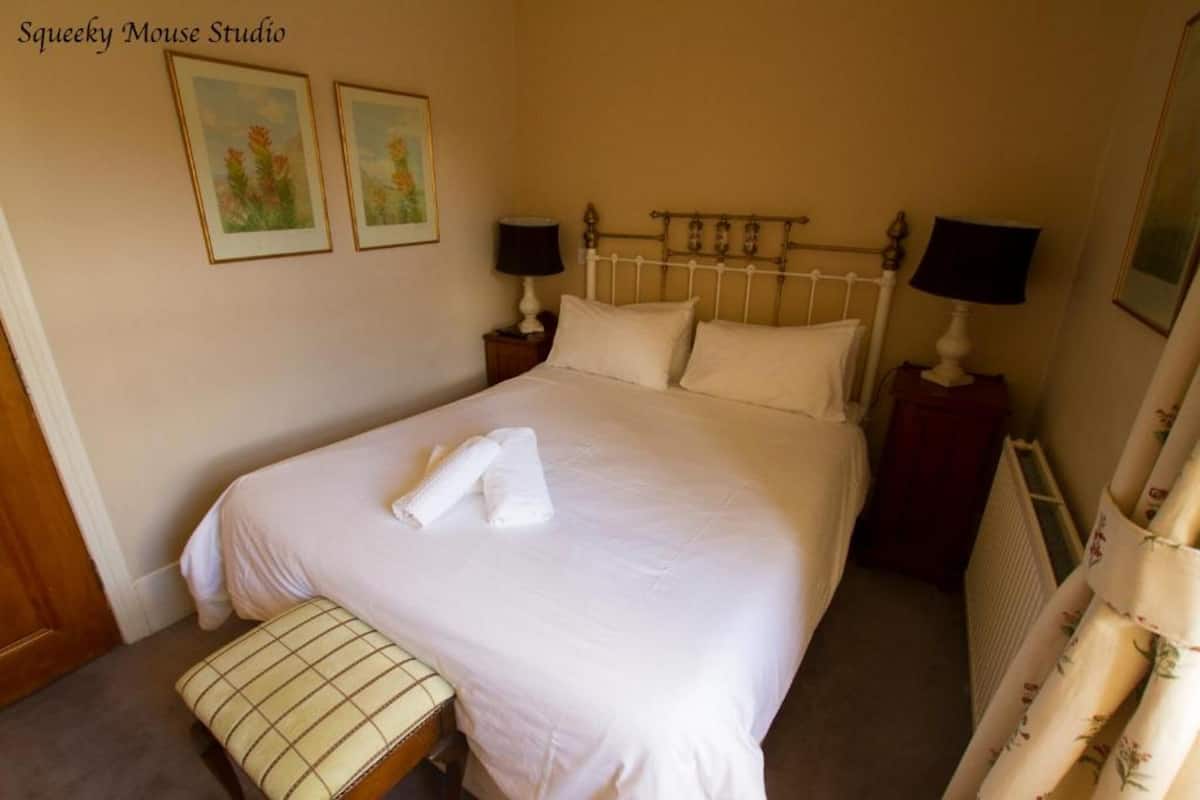 A neatly made bed with white linens and two pillows, a bedside table with a lamp, and a bench at the foot of the bed.