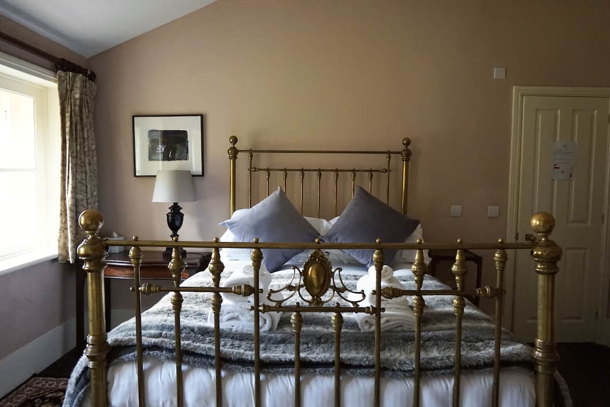 A bed with a gold frame, grey and white bedding, and two pillows.