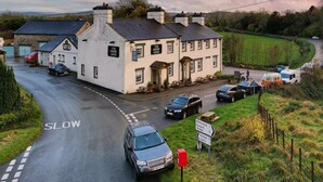 A white building with multiple chimneys, a sign reading "The Derby Arms," and a road with a 'SLOW' marking. - The Derby Arms Witherslack (Grange-over-Sands)