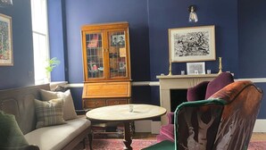 A room with a blue wall, a wooden cabinet, a sofa, a chair, and a fireplace. - The Derby Arms Witherslack (Grange-over-Sands)