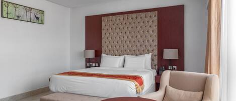 A hotel room with a bed, a chair, a round table, and a wall-mounted artwork.