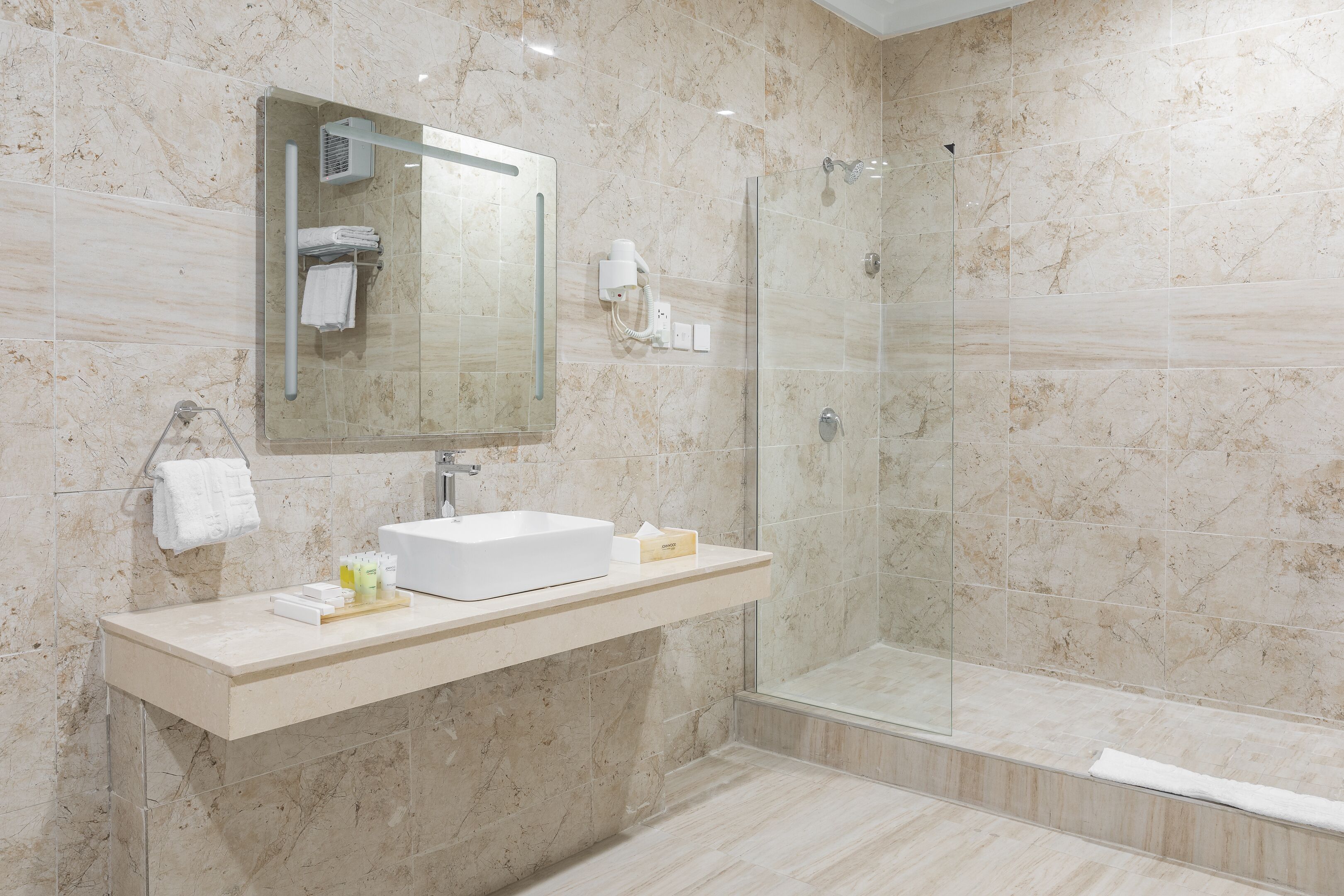 A modern bathroom with a glass-enclosed shower, a white sink, and a marble-tiled wall.
