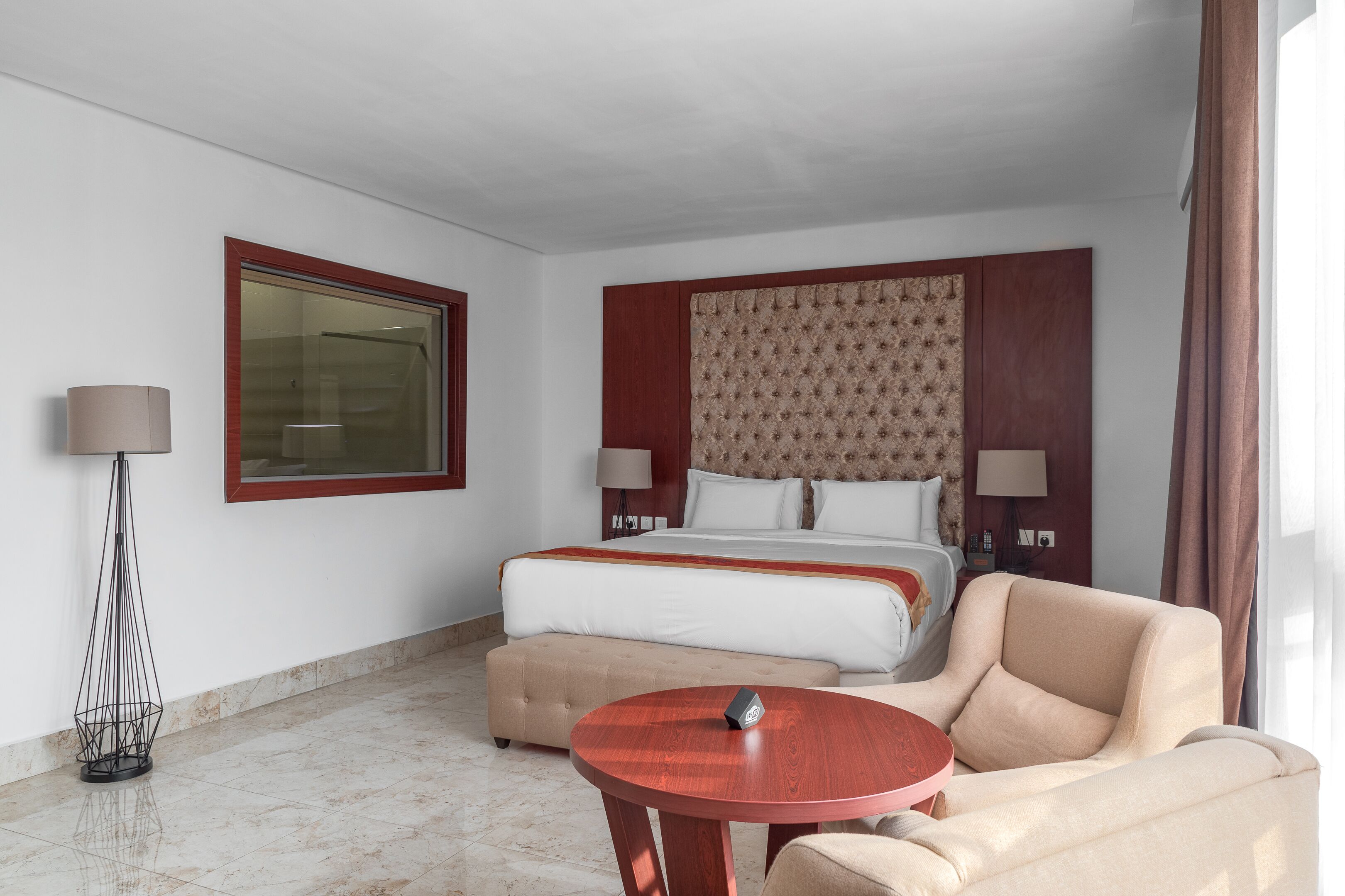 A hotel room with a bed, a sofa, a round table, a lamp, and a large window.