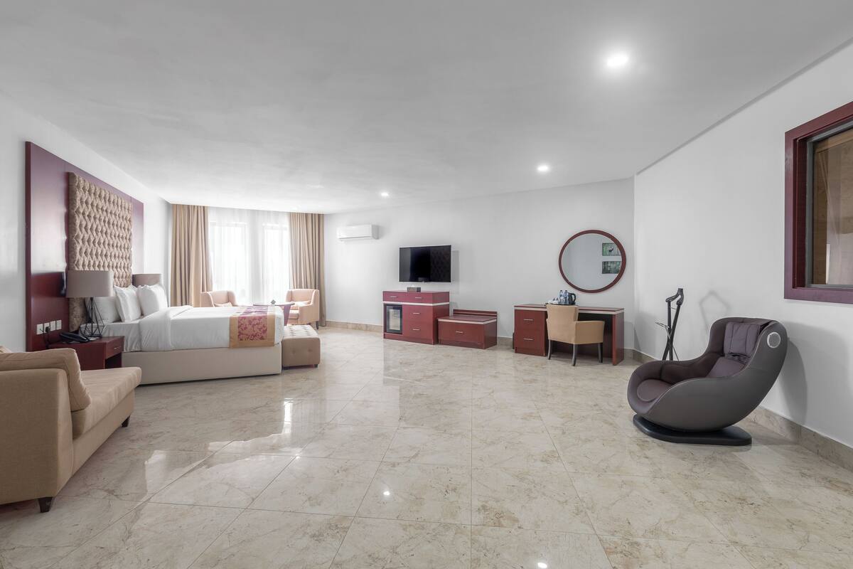 Ein modernes Hotelzimmer mit Bett, Sofa, Schreibtisch, Stuhl, Fernseher und Spiegel.