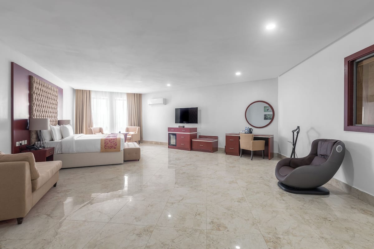A modern hotel room with a bed, sofa, desk, chair, TV, and a mirror.