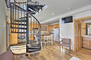 A spacious kitchen with wooden cabinets, a dining area with white chairs, and a modern black spiral staircase. - ‘Happy’s Haven’ Cabin w/ Gas Grill &  Fire Pit! (Lodi)