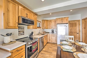 A kitchen with wooden cabinets, stainless steel appliances, and a dining area set for four. - ‘Happy’s Haven’ Cabin w/ Gas Grill &  Fire Pit! (Lodi)