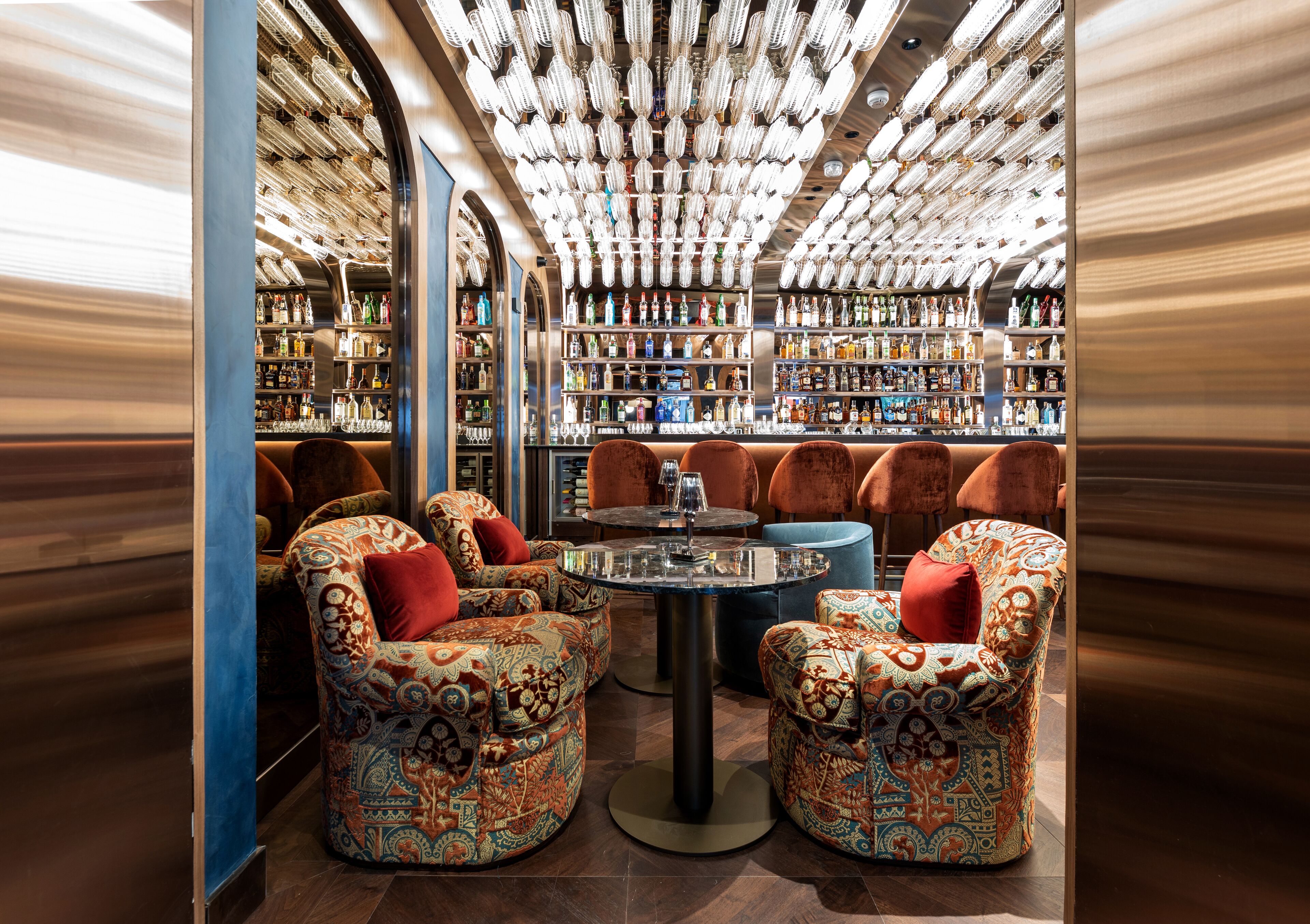 Un área de bar con sillas estampadas, una mesa central y estanterías llenas de botellas.