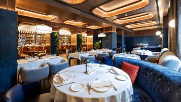 Un restaurante con mesas redondas, asientos tapizados en azul y un techo de madera con iluminación empotrada.