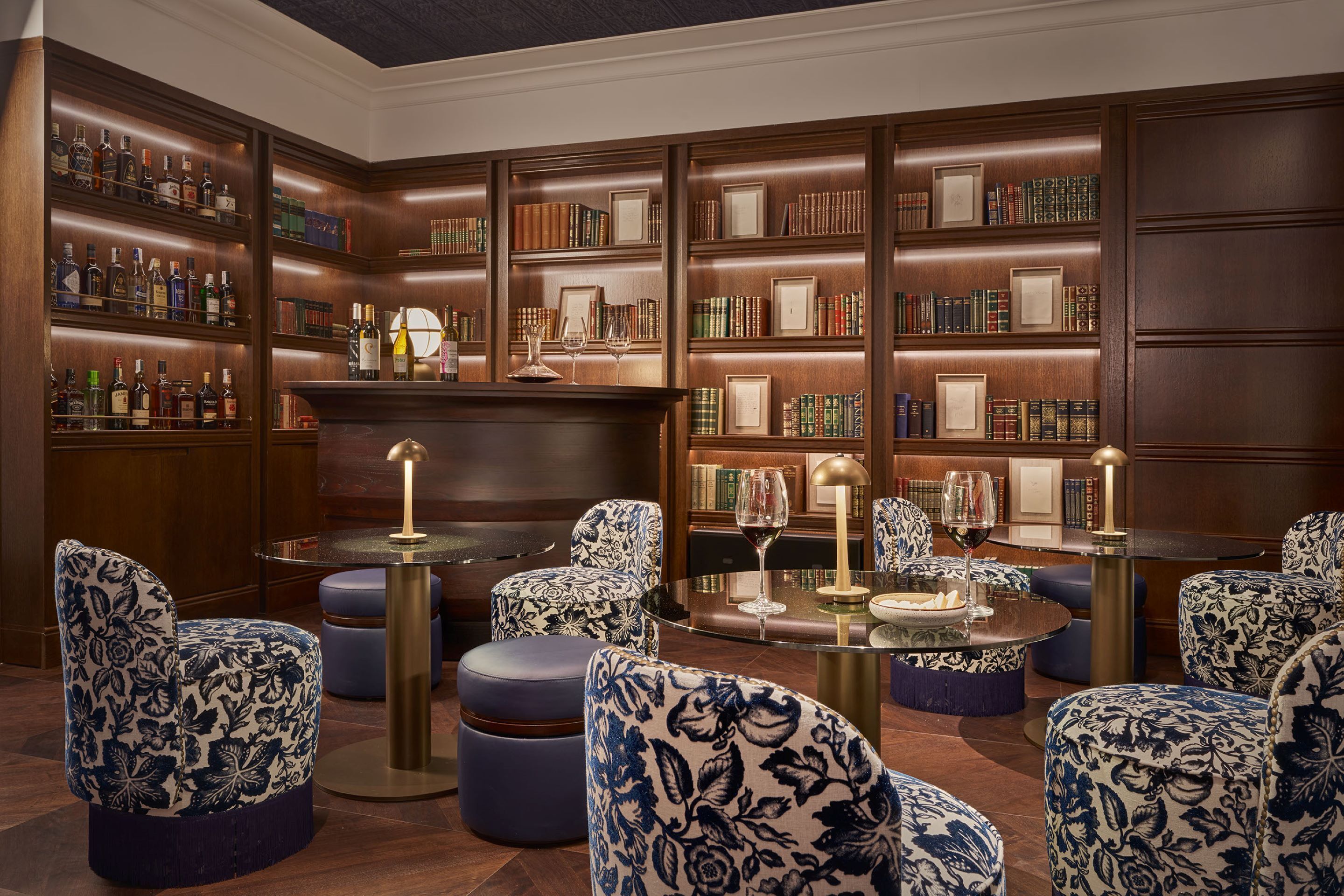Una biblioteca con estanterías, una zona de bar y asientos con una mesa de vidrio.