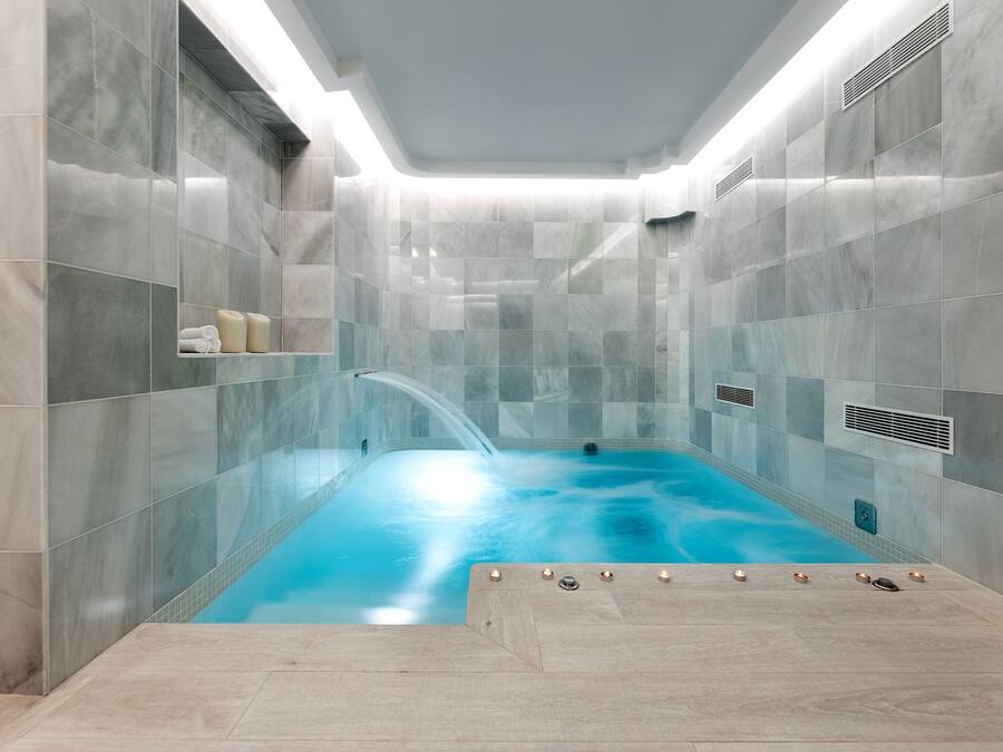 A modern spa room with a glass-enclosed hot tub, marble walls, and a wooden floor.