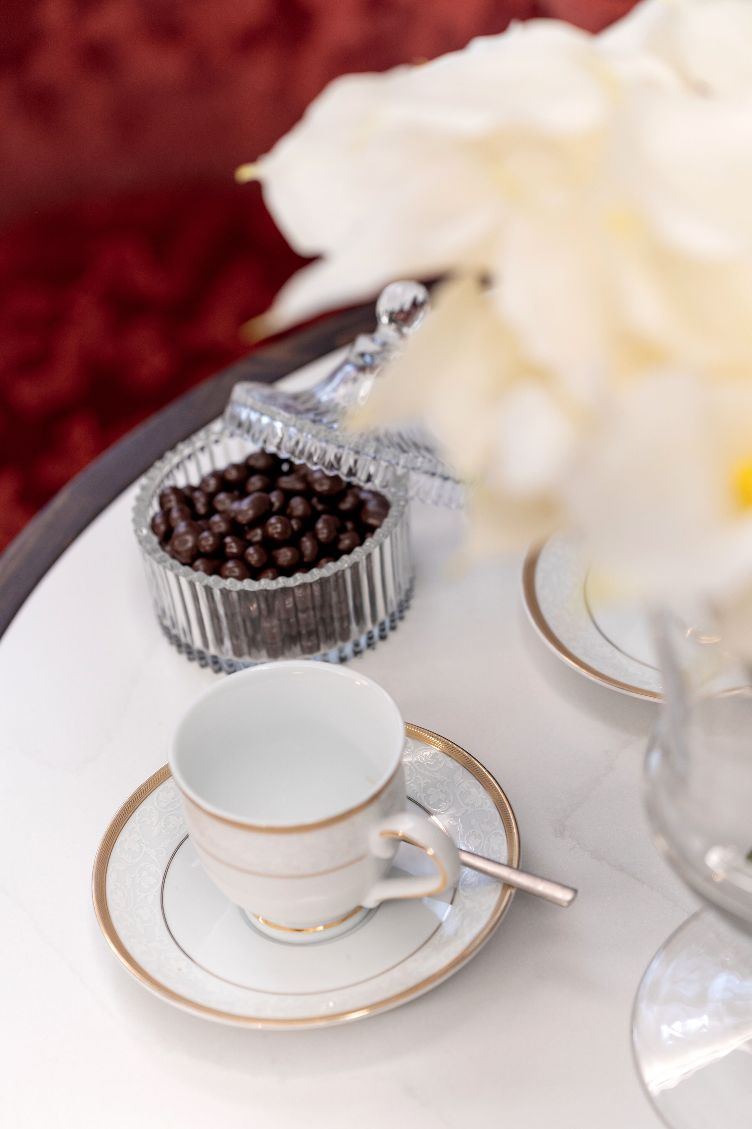 Una bandeja con una taza y platillo, un recipiente pequeño de bombones de chocolate, y un florero con flores blancas.