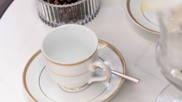 Una bandeja con una taza y platillo, un recipiente pequeño de bombones de chocolate, y un florero con flores blancas.