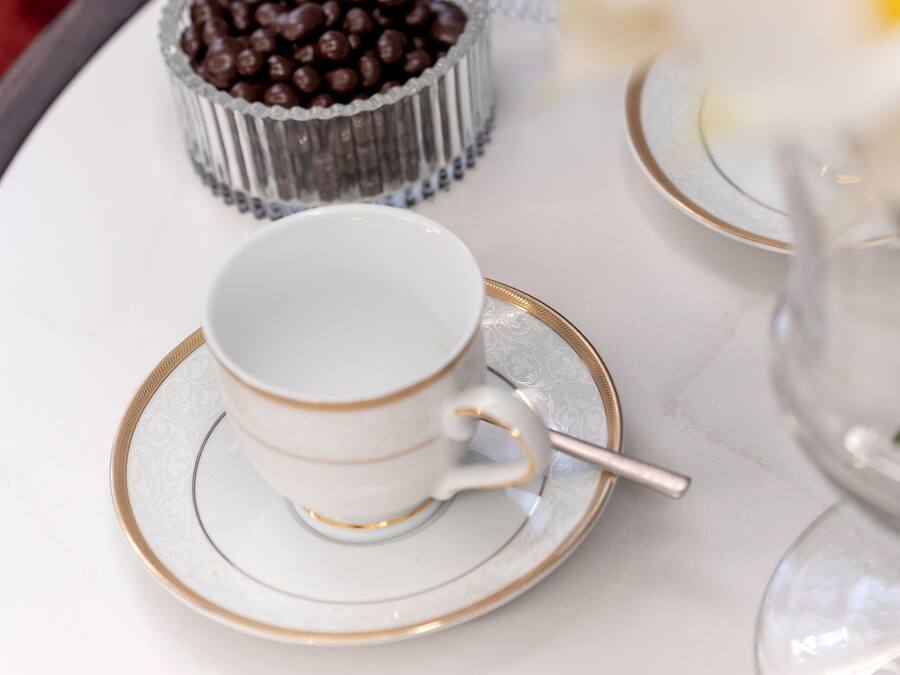 Una bandeja con una taza y platillo, un recipiente pequeño de bombones de chocolate, y un florero con flores blancas.