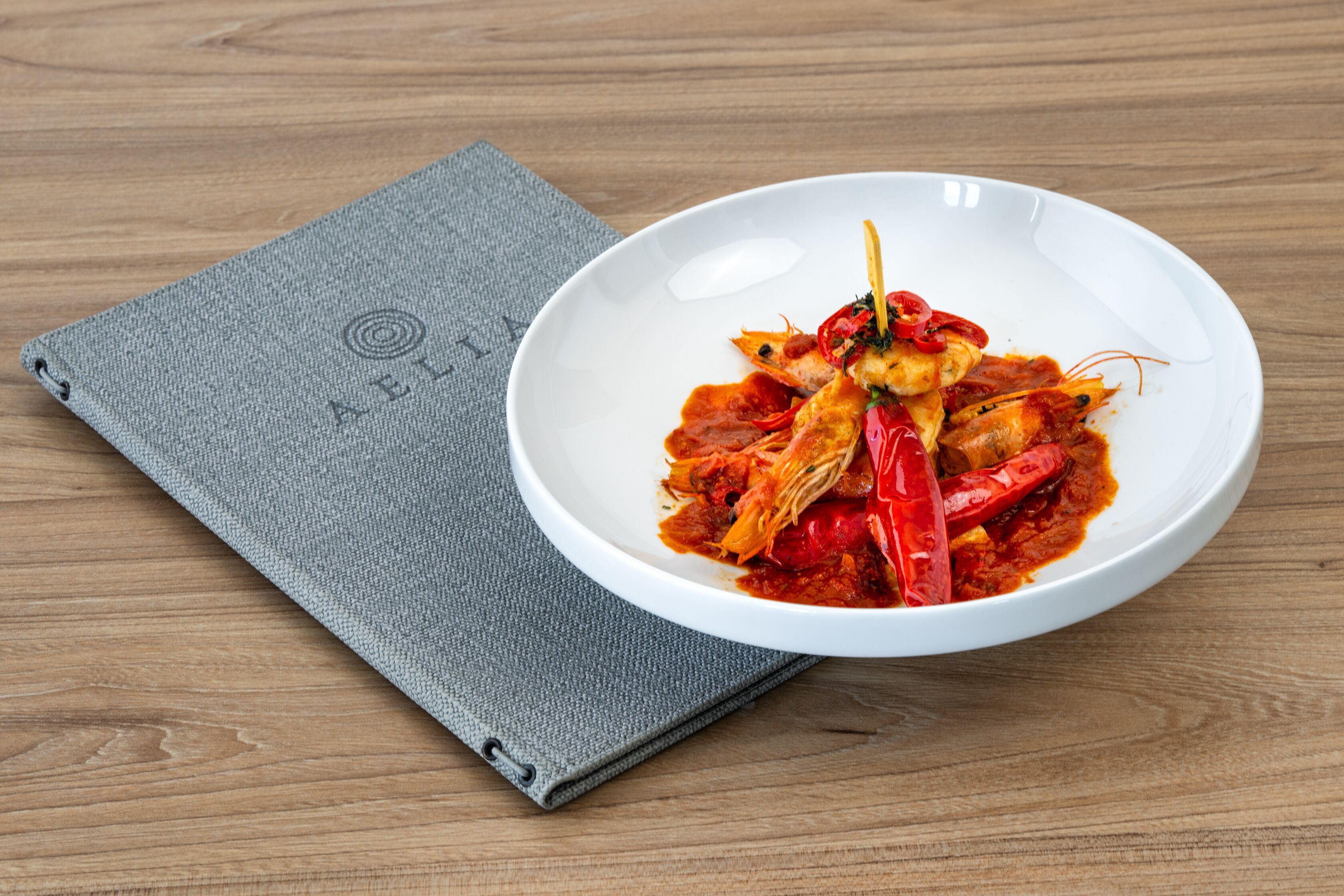 A white bowl of food with red sauce and chili peppers on a wooden table.