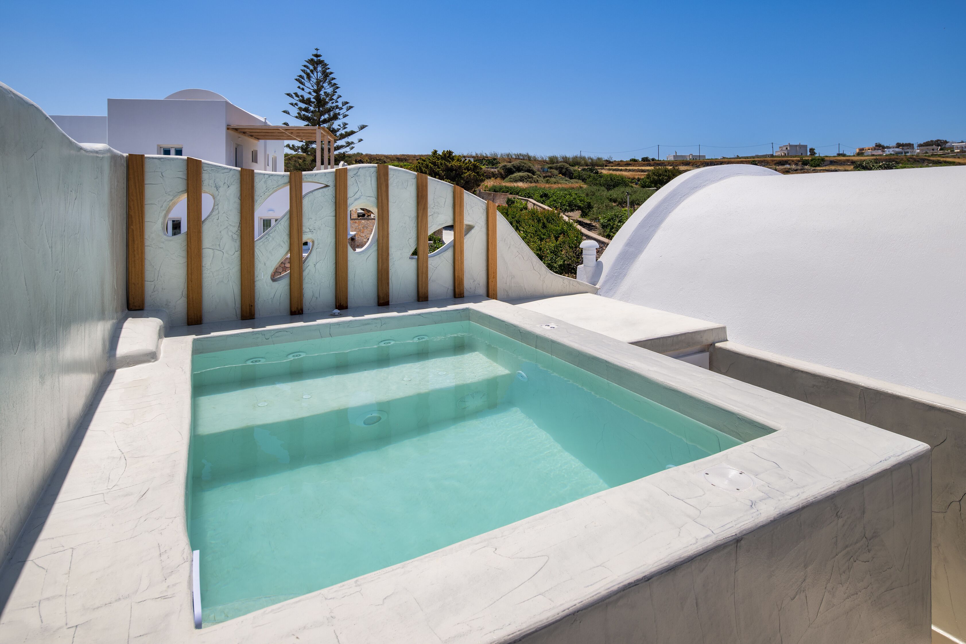 A rooftop pool with a clear blue water feature, surrounded by white walls and wooden accents.