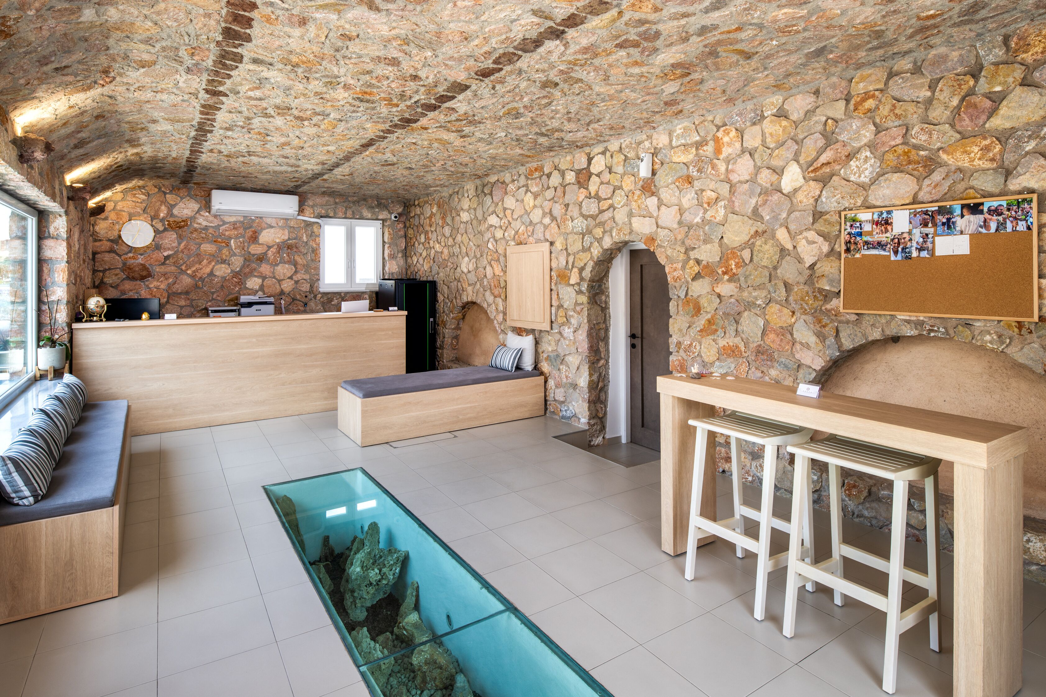 Um quarto com paredes de pedra, uma receção, área de estar e uma mesa de vidro com um objeto decorativo.