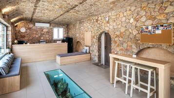 Um quarto com paredes de pedra, uma receção, área de estar e uma mesa de vidro com um objeto decorativo.