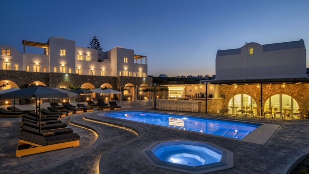 A modern outdoor pool area with lounge chairs and a hot tub, surrounded by stone walls and a bar area. - Aelia Luxury Suites (Santorini)