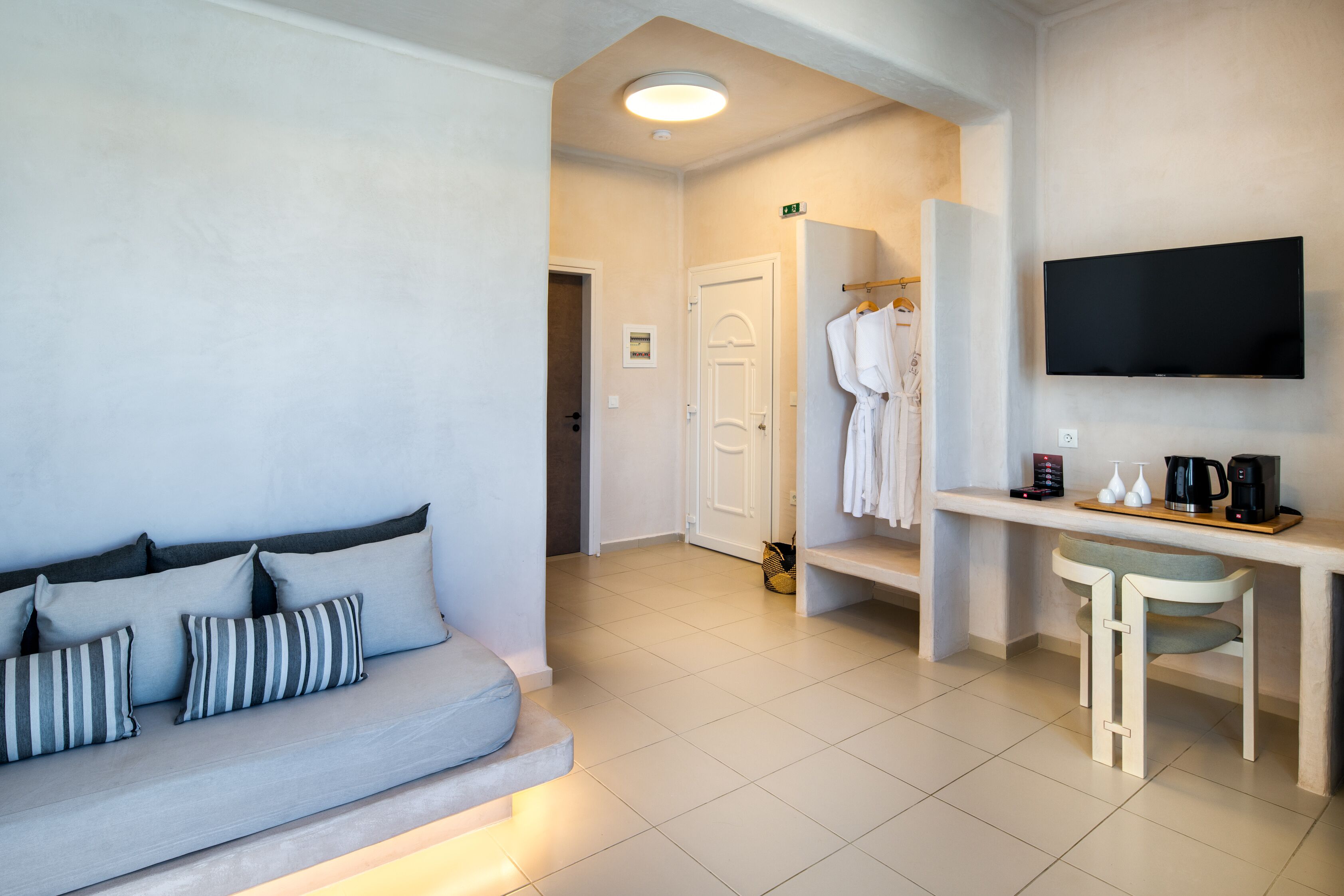 Ein Hotelzimmer mit Sofa, Fernseher, Schreibtisch mit Kaffeemaschine und Bademantel an einem Kleiderhaken.