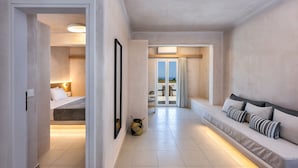 A modern hotel room with a bed, a sofa, and a view of the sea. - Aelia Luxury Suites (Santorini)